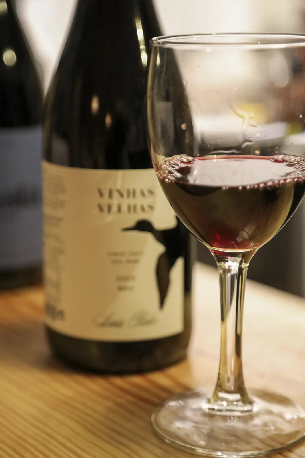 A glass of red wine and a bottle of Vinhas Velhas on the counter at Cajou
